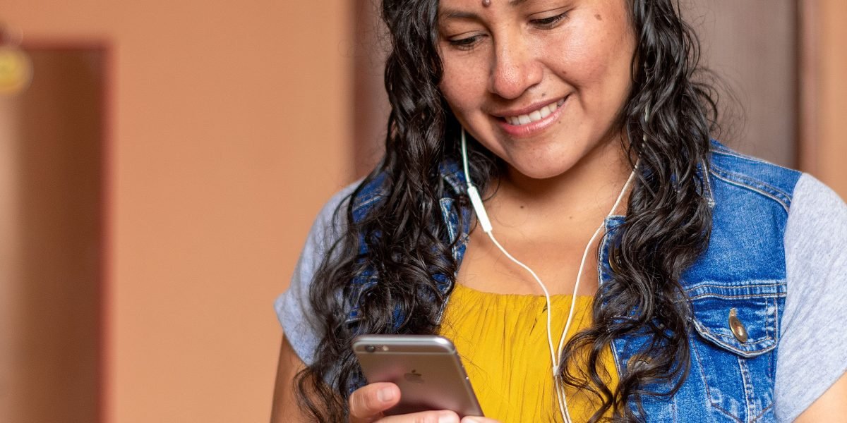 A person smiles and laughs while looking at a phone, illustrating the joy and connection derived from online humor.